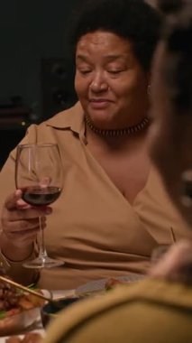 Siyahi son sınıf öğrencisi bir kadının yemek masasında ailesiyle sohbet ederken, kutlama sırasında özel bir kutlama yapmak için kadeh kaldırışının dikey çekimi.