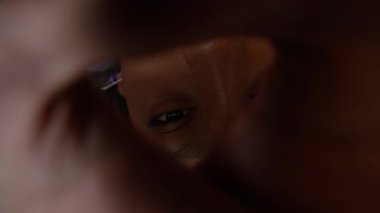 Yüksek açılı, renkli süveterli siyah bir gencin kameraya çapraz gözlerle baktığı, kapalı alanda yerde yattığı bir görüntü.