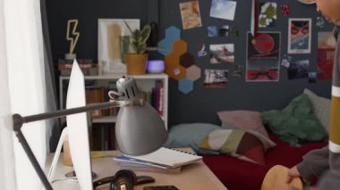 Afrika kökenli Amerikalı bir gencin masa lambasını açarken, bilgisayar başında otururken, kulaklık takarken ve odasında ödev yaparken elde çekilmiş bir fotoğrafı.