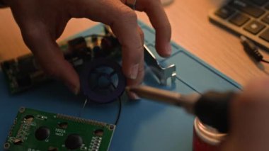 Yüksek açılı, devre kartında lehimleme çipleri kullanan, lehimleme demiri kullanan, masa üzerinde çalışan ve hasarlı parçaları tamir eden tanınamaz hale gelmiş elektrikçi ellerinin görüntüsü.