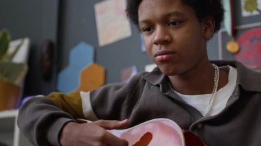 Düşünceli Afro-Amerikalı gencin evde gitar çalışmasını yavaş yavaş çekiyoruz.