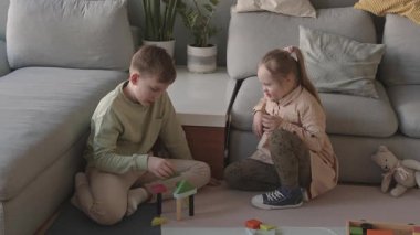 Beyaz çocuğun oturma odasında halıda oturup oyuncak inşaat setini kullanarak şato inşa ederken Down sendromlu bir kızın onu izlemesi ve sonra da inşaatını yerle bir etmesi.