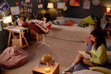 İki arkadaş, kişisel eşyalarla dolu, güzel dekore edilmiş bir yatak odasında ders çalışıyor. Biri masada otururken diğeri yatakta kitap okuyor ve sıcak ve odaklanmış bir atmosfer yaratıyor.