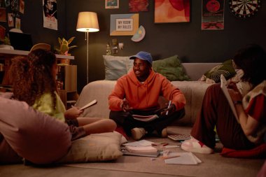 Çalışma materyalleriyle çevrili yerde oturan bir grup arkadaş sohbete daldılar ve görevlerde işbirliği yaptılar. Ilık ışıklandırma ve gelişigüzel kurulum rahat bir atmosfer yaratır.