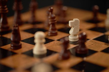 Ahşap satranç tahtasındaki satranç taşlarının yakın plan görüntüsü stratejik konumlandırmayı vurguluyor. Bu klasik masa oyunundaki zarafet ve hassasiyeti gözler önüne seriyor.