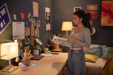 Çalışma odasının yakınındaki rahat, dekore edilmiş, etrafı resimler ve dekorlarla çevrili, masa aydınlatma alanında bir lambayla çalışan bir kadın.