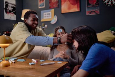 Oturma odasında, masa oyunları ve sıcak bir atmosferle etkileşimli bir oyun oynayan bir grup arkadaş.