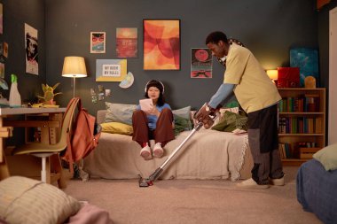 Sıcak yatak odasını birlikte süpürerek genç bir kıza yardım etmek bir adamın yatakta oturup kitap okurken temizlik yaptığını gösteriyor. Ev işleri ile meşgul olarak ortaya çıkan oda dekorasyonu rahat bir ortam sunuyor