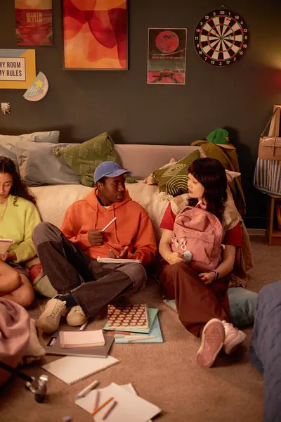 Bir grup arkadaş sıcak yurt odasında oturmuş masa oyunları ve kitapların etrafında gevşeyip sohbet ediyorlar. Canlı dekor elementleri rahat, davetkar bir atmosfer yaratır.