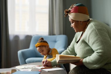 Afro-Amerikalı olgun bir kadının küçük şirin bir kıza alfabe öğretirken çekilmiş minimal bir yan görünüm portresi.