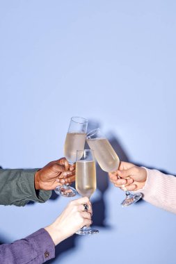 Şenlik kutlamalarında şampanya kadehleriyle kadeh kaldıran bir grup insan. Farklı ırkların elleri, arka planda sade ışığa karşı görünür. Birlik ve neşeyi vurguluyorlar.