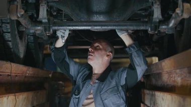 Orta ölçekli, orta yaşlı, beyaz tenli tamirci araba kamyonunun altında dikilirken ve oto tamirhanesinin alt kısımlarını tamir ederken.