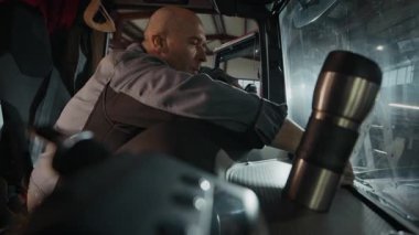 Orta yaşlı, beyaz bir adamın, garajdaki kamyon kabininin içindeki bez temizleme kamyonuyla toz temizlerken çekilmiş bir fotoğrafı.