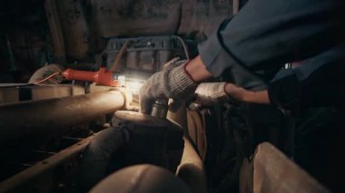 Pamuk eldivenli tanınmayan araba tamircisinin loş ışıklı otomobil tamirhanesinde aracı tamir ederken çekilmiş görüntüsü.