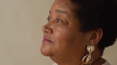 Kısa kıvırcık saçlı ve kameraya gülümseyen yaşlı Afrikalı Amerikalı kadının yakın plan portresinin üstünden.