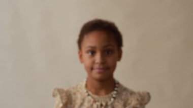 Kısa kıvırcık saçlı genç Afro-Amerikalı kızın yakın plan portre fotoğrafını çek. Kameraya bakıyor. Üstü başı desenli ve kolyesi boncuklu.