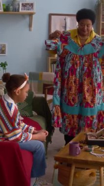 Afro-Amerikan büyükannenin elbise denerken ve torunuyla rahat oturma odasında tartışırken çekilmiş dikey bir fotoğrafı.