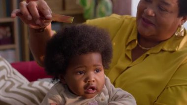 Afro-Amerikan büyükannesini seven küçük torununun saçlarını nazikçe tarayan rahat ve renkli bir oturma odasında