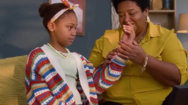 Genç Afrikalı Amerikalı kızın oturma odasında kanepede otururken büyükannesiyle aksesuar denemesi.