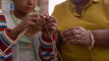 Tanımlanamayan Afro-Amerikalı bir kadının, örgü örmesini öğretirken, rahat bir oturma odasında otururken yakın plan çekimleri.