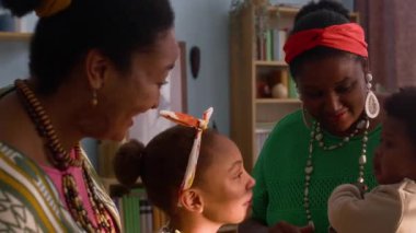 İki Afrikalı Amerikalı kadın, genç kız ve bebek sıcak, neşeli anı paylaşıyor, rahat oturma odasında birlikte gülüyor ve oynuyorlar.