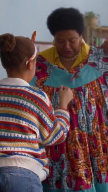 Afro-Amerikan büyükannesinin torununa rahat oturma odasında elbisesini birlikte seçmesini isterken çekilmiş dikey bir fotoğrafı.