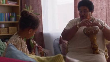 Torunu rahat oturma odasında ukulele çalarken Afrikalı Amerikalı bir kadının şarkı söyleyip davul çalması.