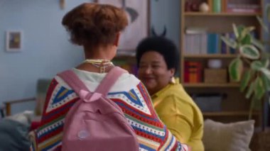 Afrikalı Amerikalı kız büyükannesine sarılmak için koşuyor, küçük kız kardeşine bakıyor, rahat bir oturma odasında kanepede oturuyor.