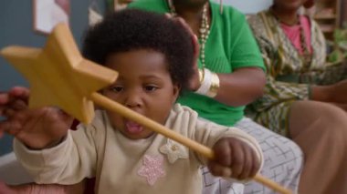 Annesi ve teyzesi oturma odasında kanepede otururken Afro-Amerikan bebek tahta oyuncakla oynuyordu.