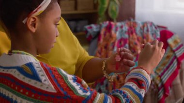 Afro-Amerikalı bir kadının torununa mücevherlerini gösterip oturma odasındaki kanepede otururken çekilmiş fotoğrafı.