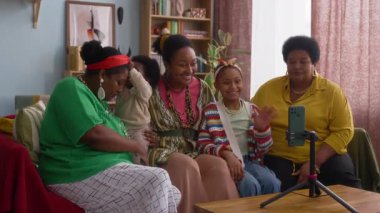 Bebek ve çocuğun da içinde olduğu beş kişi, rahat oturma odasındaki tripodda akıllı telefon kullanarak video çağrısı için el sallıyorlar.