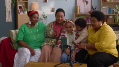 Beş kişilik neşeli bir aile, renkli giysiler içinde, rahat oturma odasındaki tripodla akıllı telefonun etrafında toplandılar.