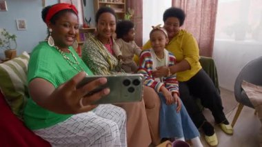 Büyük ve mutlu bir Afrikalı Amerikalı çiftin renkli oturma odasındaki kanepede selfie çekerken yüksek açı çekimi.