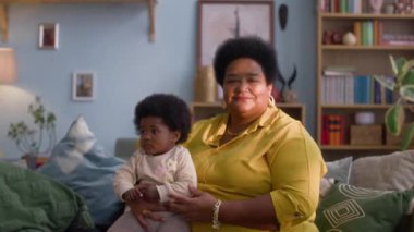 Afro-Amerikan bir büyükannenin portre fotoğrafı. Kanepede oturuyor ve kucağında bebek var.