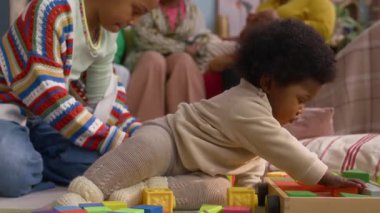 Afro-Amerikalı çocuk, ablasıyla renkli bloklar oynarken, rahat oturma odasında yerde oturuyor.