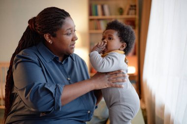 Küçük bebek yatak odasında kanepede dikilirken, Siyah Anne 'nin kızı nazikçe kucakladığı orta boy bir fotoğraf.