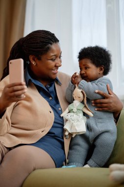 Küçük kızıyla birlikte oturma odasındaki koltukta otururken, el yapımı pelüş tavşan oyuncağını tutan mutlu bir kız bebek.