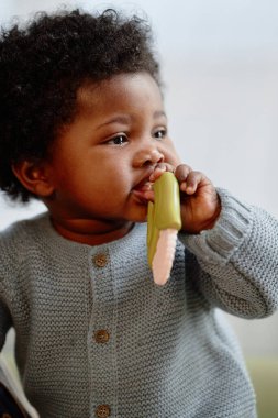 İç mekânda yakalanan ilk diş büyümesini yaşayan, rahat örülmüş tulum giymiş, dişlek bir kızın dikey portresi.
