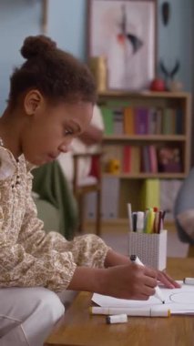 Torunuyla ilgilenen Afro-Amerikan bir kadının dikey resmi. Kahve masasında, rahat bir oturma odasında keçeli kalemle çizim yapıyor.