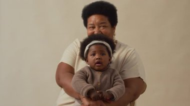 Şefkatli ve sevecen Afrikalı Amerikalı büyükannenin portresi küçük torununu kucaklıyor ve kameraya gülümsüyor.