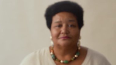 Afrika kökenli, kısa, kıvırcık siyah saçlı, büyük küpeli ve boncuklu kolyeli bir kadının kameraya bakarken yakın plan fotoğrafını çek.