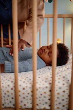 Uyuyan siyah kızın beşiğine dikey bir atış. Beşikte yatan siyah kız, beşiğinde küçük kızını kontrol ederken şefkatli annesi yatak odasında uyurken.