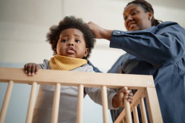 Sevimli siyah kızın tahta beşikte dikilirken, annesinin çocukları nazikçe taradığı, yatak odasında kıvırcık saçlarını taradığı düşük açılı bir kare.