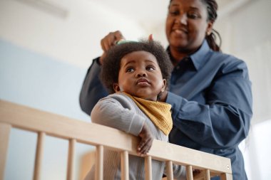 Sevimli siyah bir kızın tahta bir beşikte dikilip kameradan kafasını çevirdiği, şefkatli bir annenin çocuklarına yatak odasında kıvırcık saçlar taradığı düşük açılı bir kare.