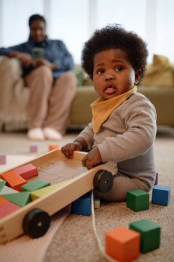 Oturma odasında yerde otururken taş ve ahşap arabalarla oynayan tatlı siyah kız çocuğunun dikey çekimi.