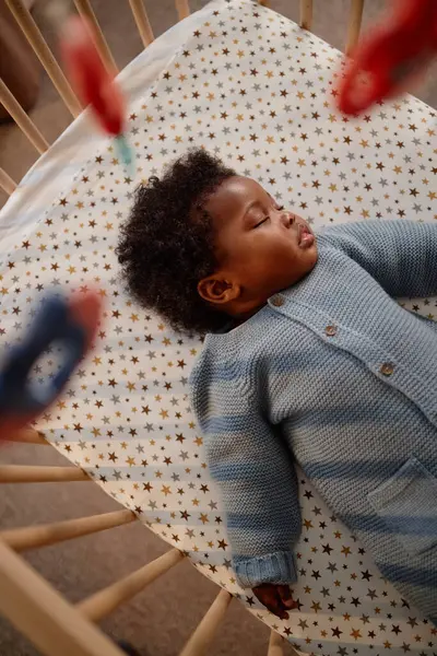 Küçük siyahi kızın bebek karyolasında uyuduğu ve çocukların yatak odasındaki cep telefonlarının üzerinde asılı olduğu dikey Hollanda açılı bir fotoğraf.