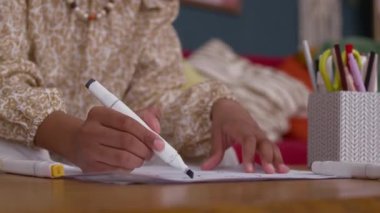 Odaklanmış Afrikalı Amerikalı kızın, rahat oturma odasında keçeli kalemlerle kağıda çizdiği düşük açılı, eğik çekim.