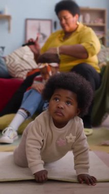 Büyükannesi ablasının saçlarını tararken Afrikalı Amerikalı bebeğin yerde sürünüp yukarı baktığı dik açılı bir fotoğraf.