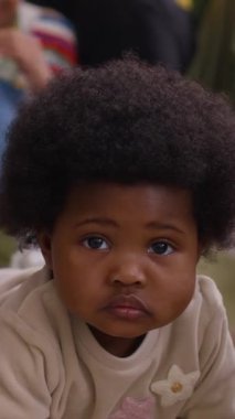 Sevimli Afrikalı Amerikalı çocuğun dikey portresi. Yerde oturmuş kameraya bakıyor.