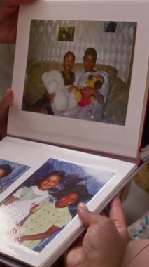 Albümdeki eski aile fotoğraflarına bakıp evde oturma odasında oturan tanınmayan üç kişinin dikey çekimi.